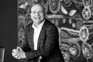 Black and white corporate portrait of CEO in front of indigenous artwork